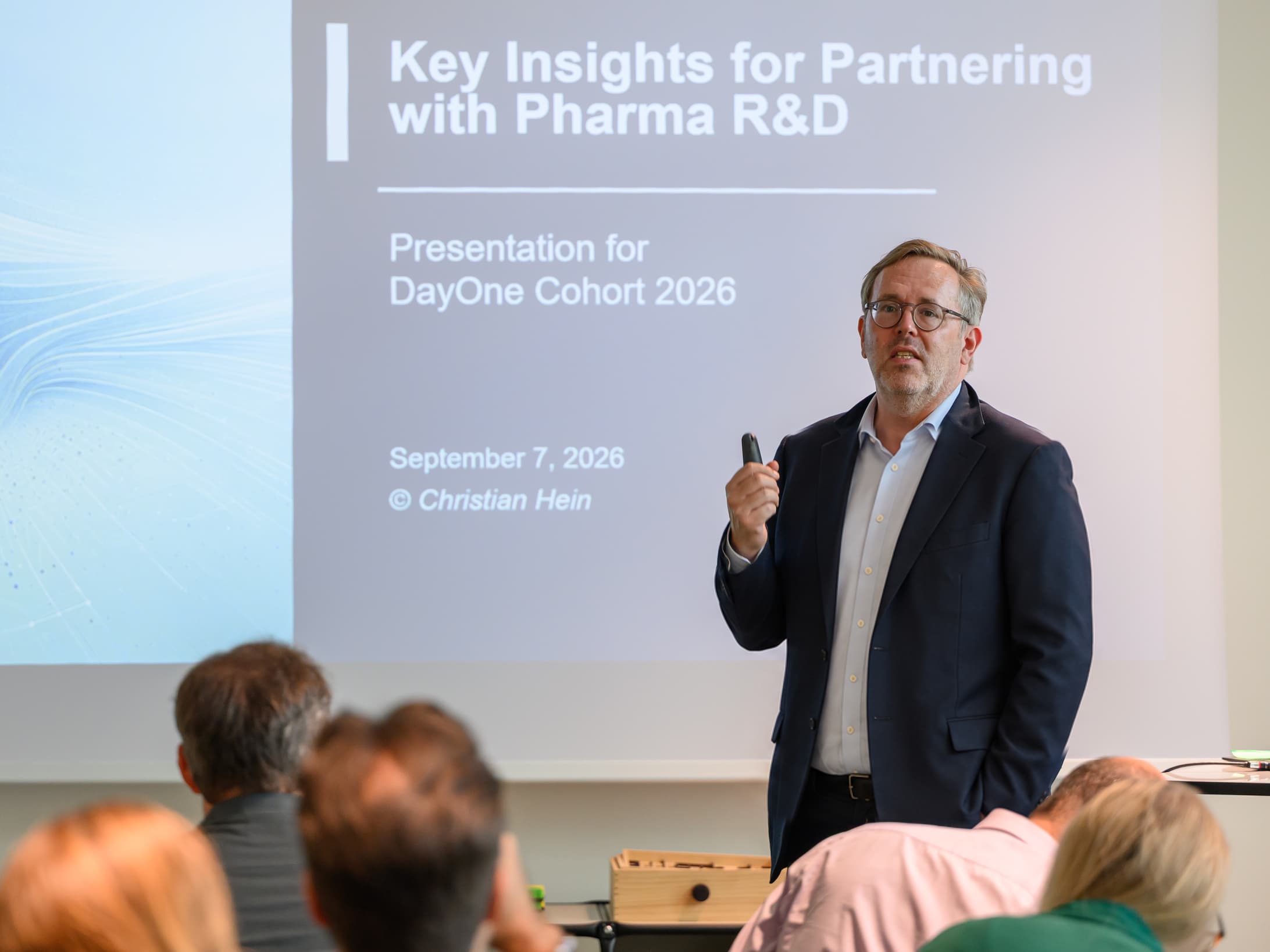 Presenting lessons on partnering with pharma R&D to the DayOne 2026 cohort, with the audience and presentation slide visible.